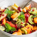 A bowl filled with a winter fruit salad including sliced pears, apples, kiwi, and pomegranate.