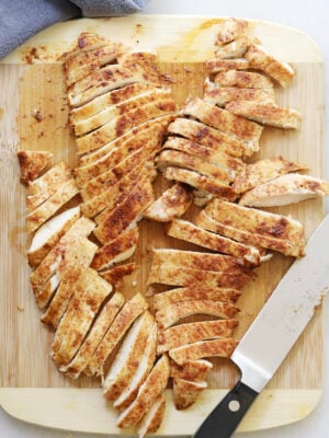 Sliced chicken marinated in a Mexican marinade, displayed on a cutting board with a knife.