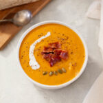 A bowl of soup with bread and bacon.