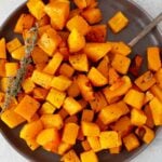 Air-fryer butternut squash on a plate with sprigs of thyme and a fork.