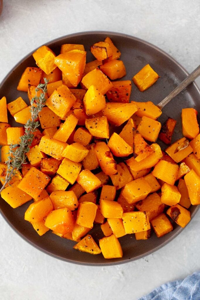 Air-fryer butternut squash on a plate with sprigs of thyme and a fork.