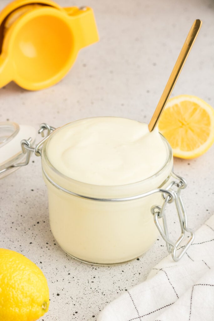 A jar of avocado oil mayo with a golden spoon, accompanied by fresh lemons and a juicer.