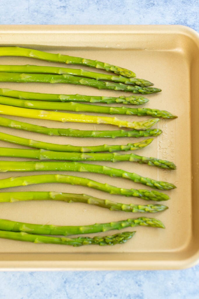 Fresh asparagus stalks on a beige tray.