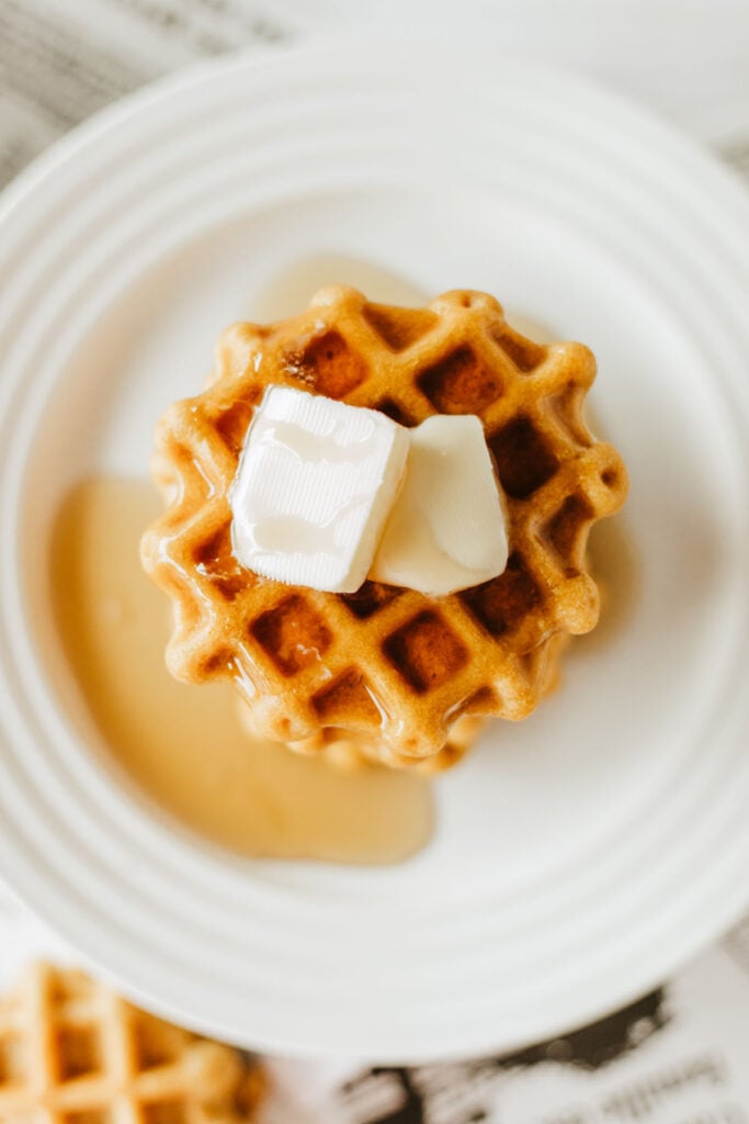 A freshly baked 2 ingredient waffle topped with butter and maple syrup, viewed from overhead.