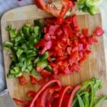 Chopped and sliced red and green bell peppers on a wooden cutting board with a knife.
