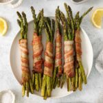 A plate of bacon-wrapped asparagus accented by lemon wedges.