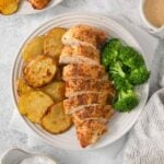 A plate with sliced, air-fried grilled chicken breast, roasted potato slices, and steamed broccoli.