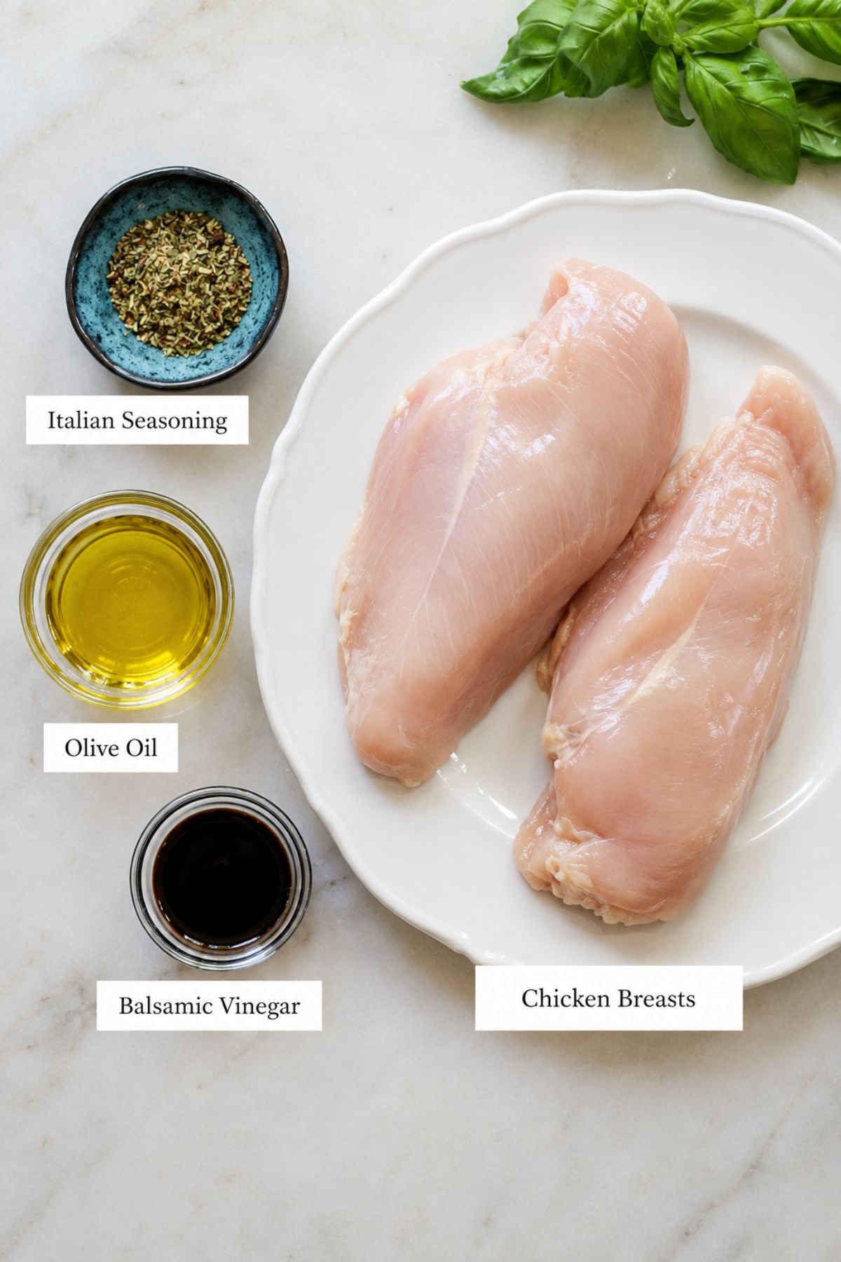 Two raw chicken breasts on a white plate beside small bowls of Italian seasoning, olive oil, and balsamic vinegar, with fresh basil leaves in the background—perfect for preparing flavorful bruschetta chicken.