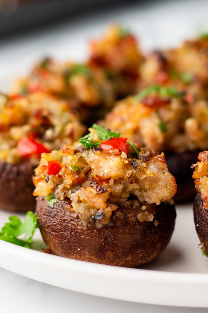 Close-up of stuffed mushrooms with minced vegetables and herbs, served on a white plate.