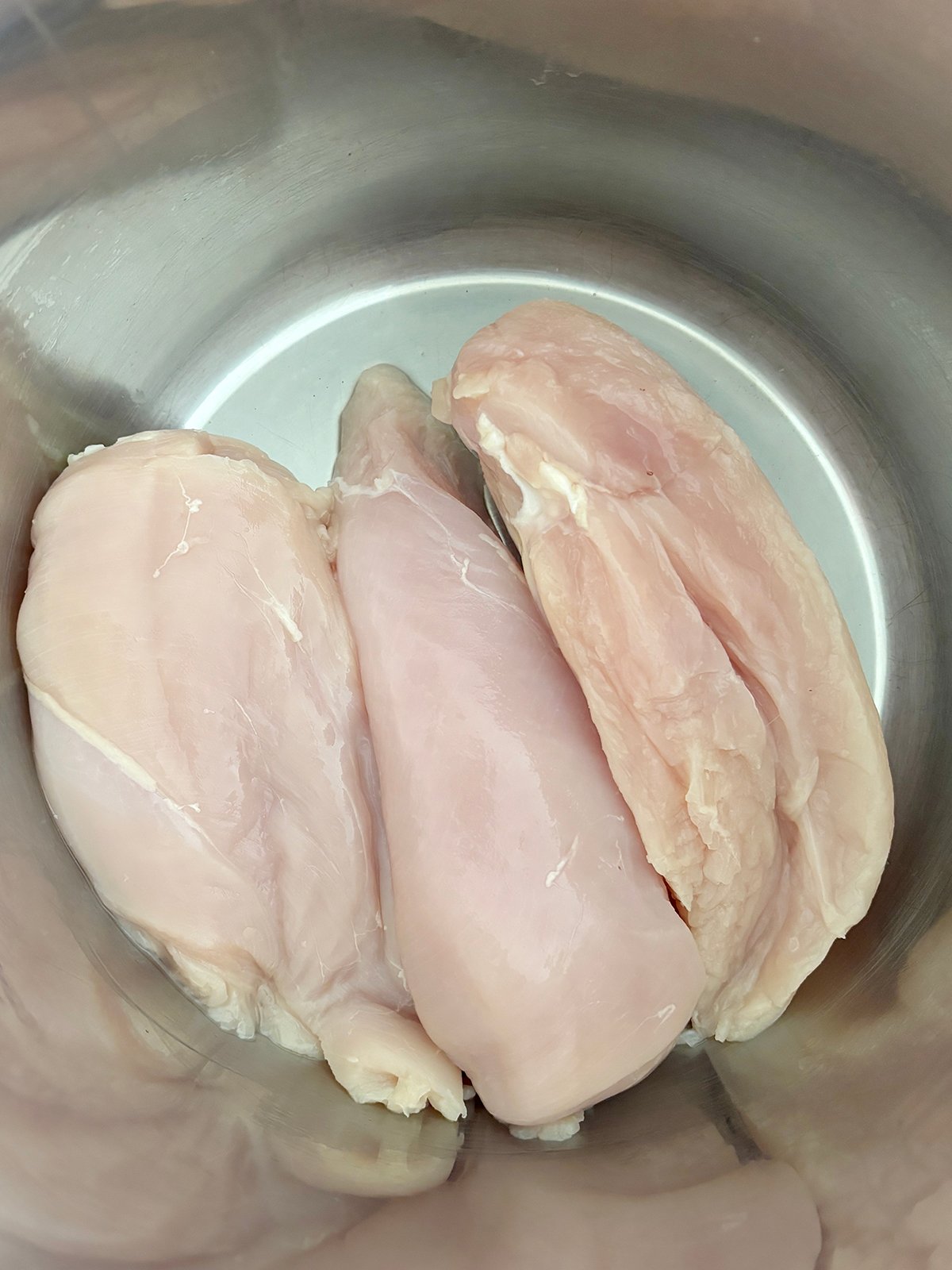 Three raw chicken breasts placed at the bottom of a metallic pot.