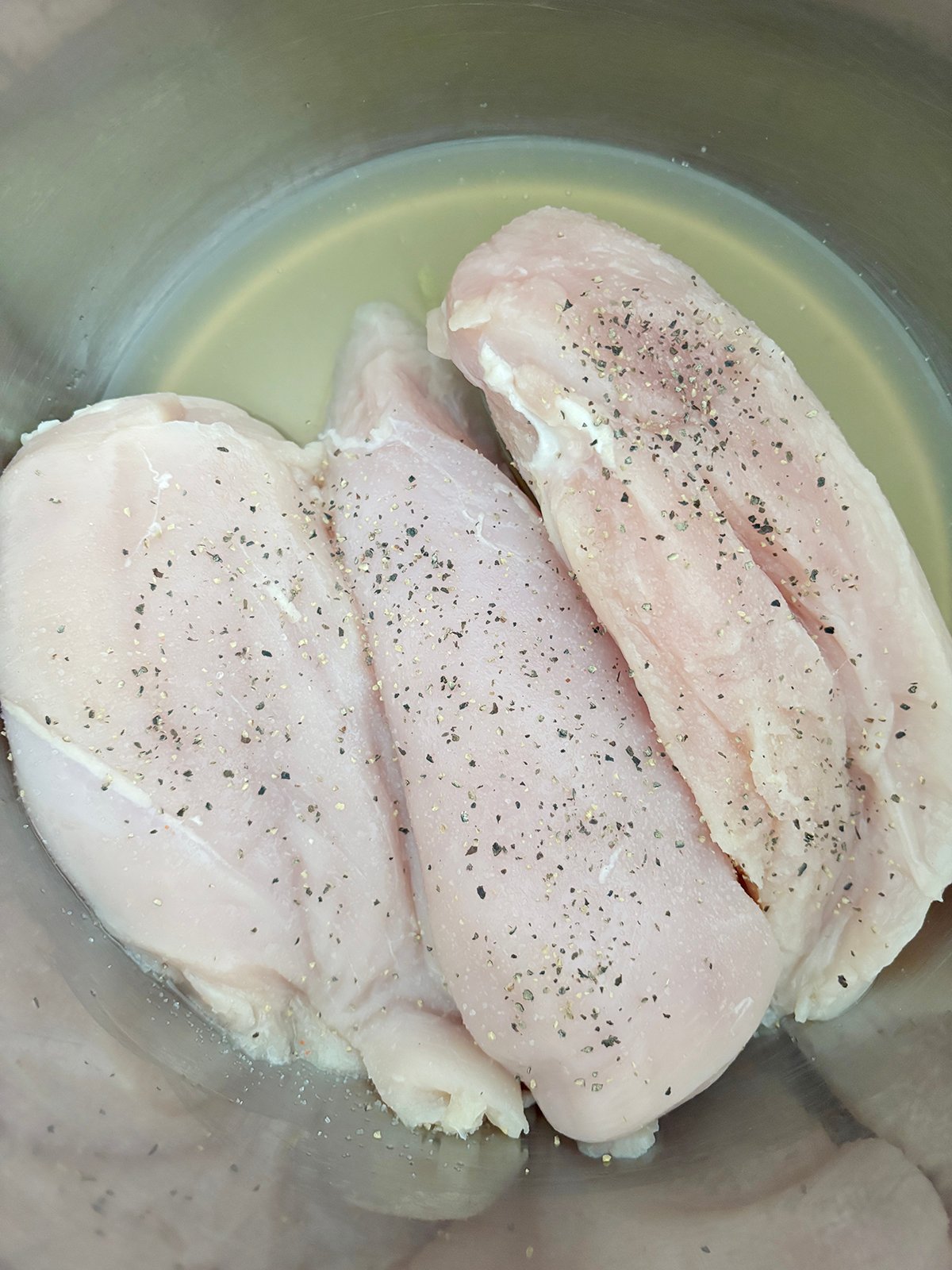 Three raw chicken breasts in an Instant Pot with chicken broth.