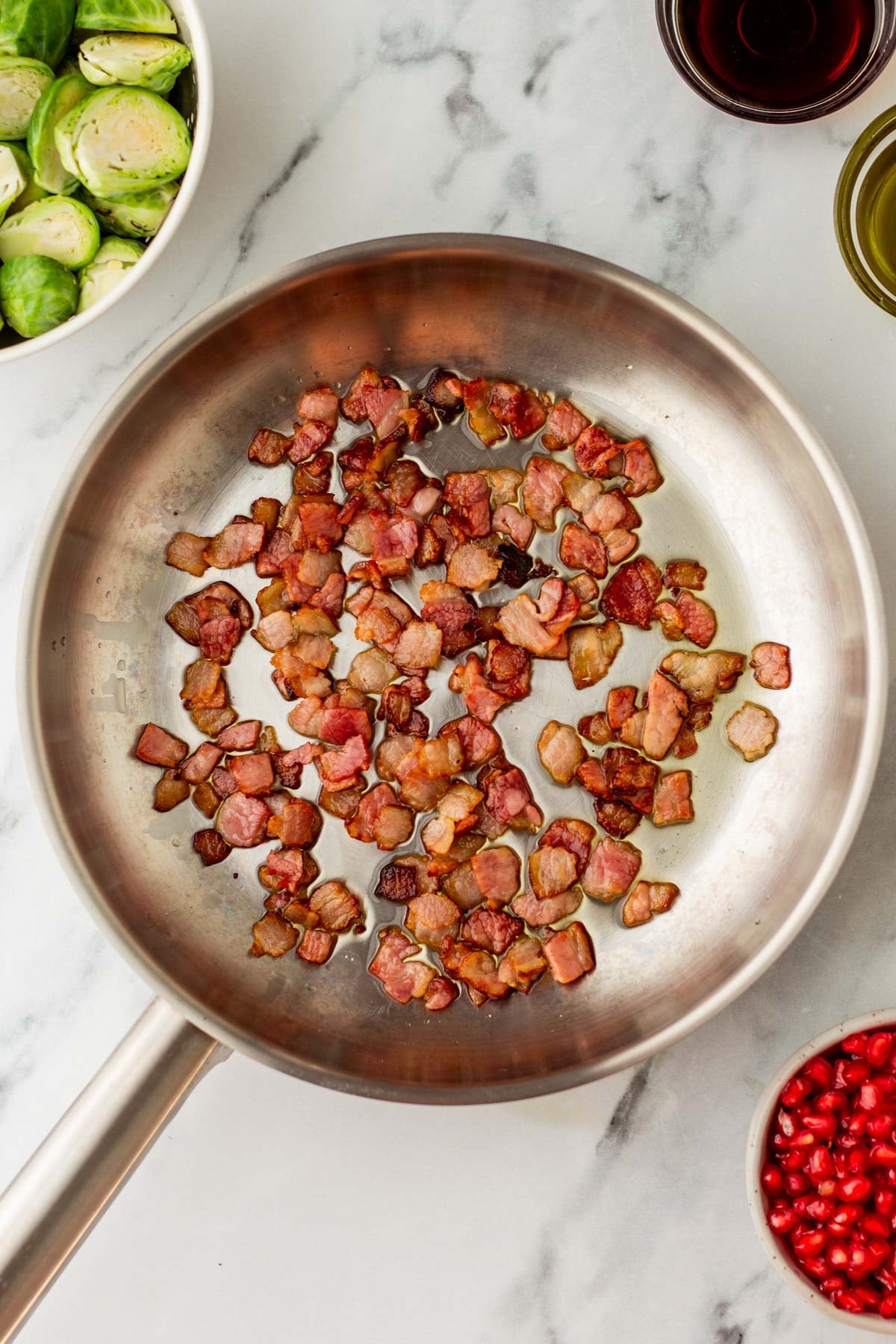 A skillet of diced, cooked bacon sits on a marble countertop.