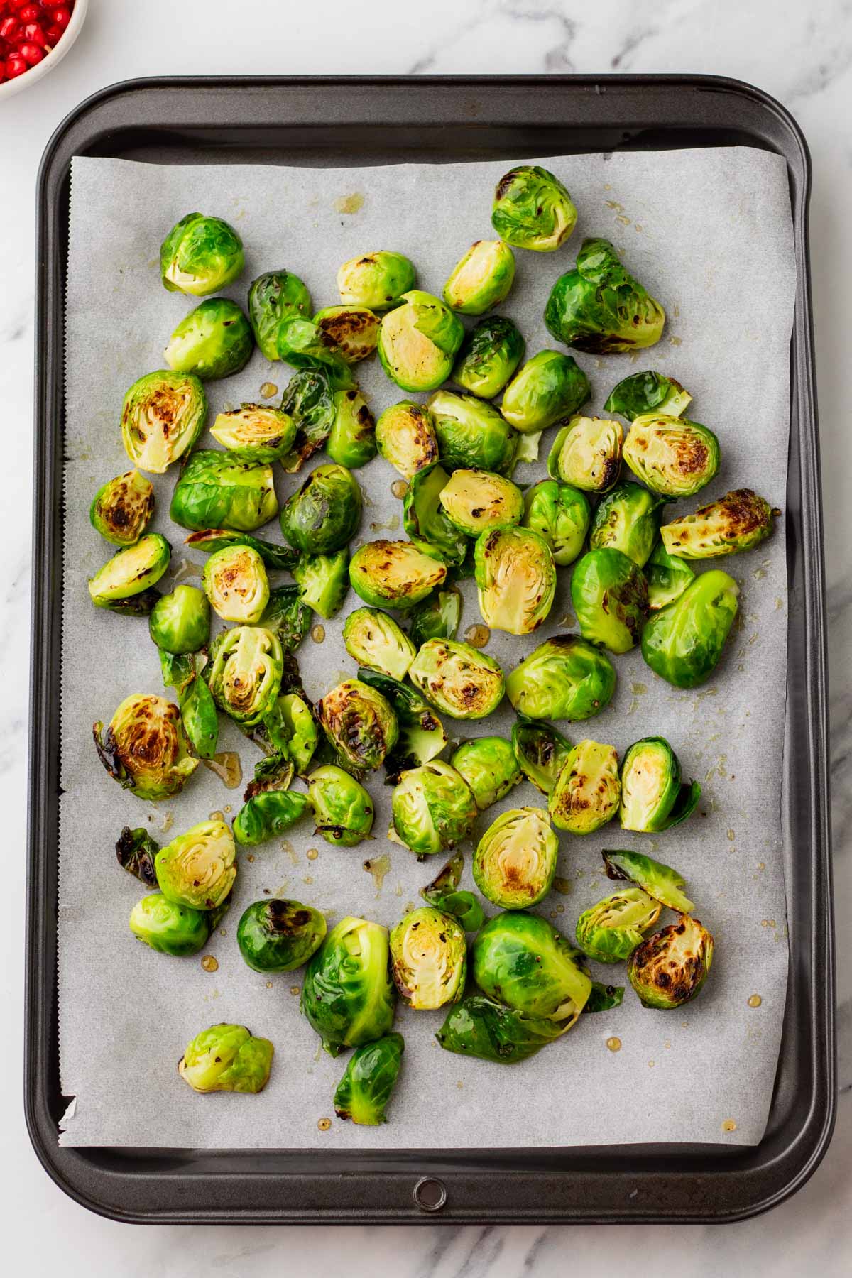 A baking tray with parchment paper is filled with roasted Brussels sprouts, some pieces showing charred edges.