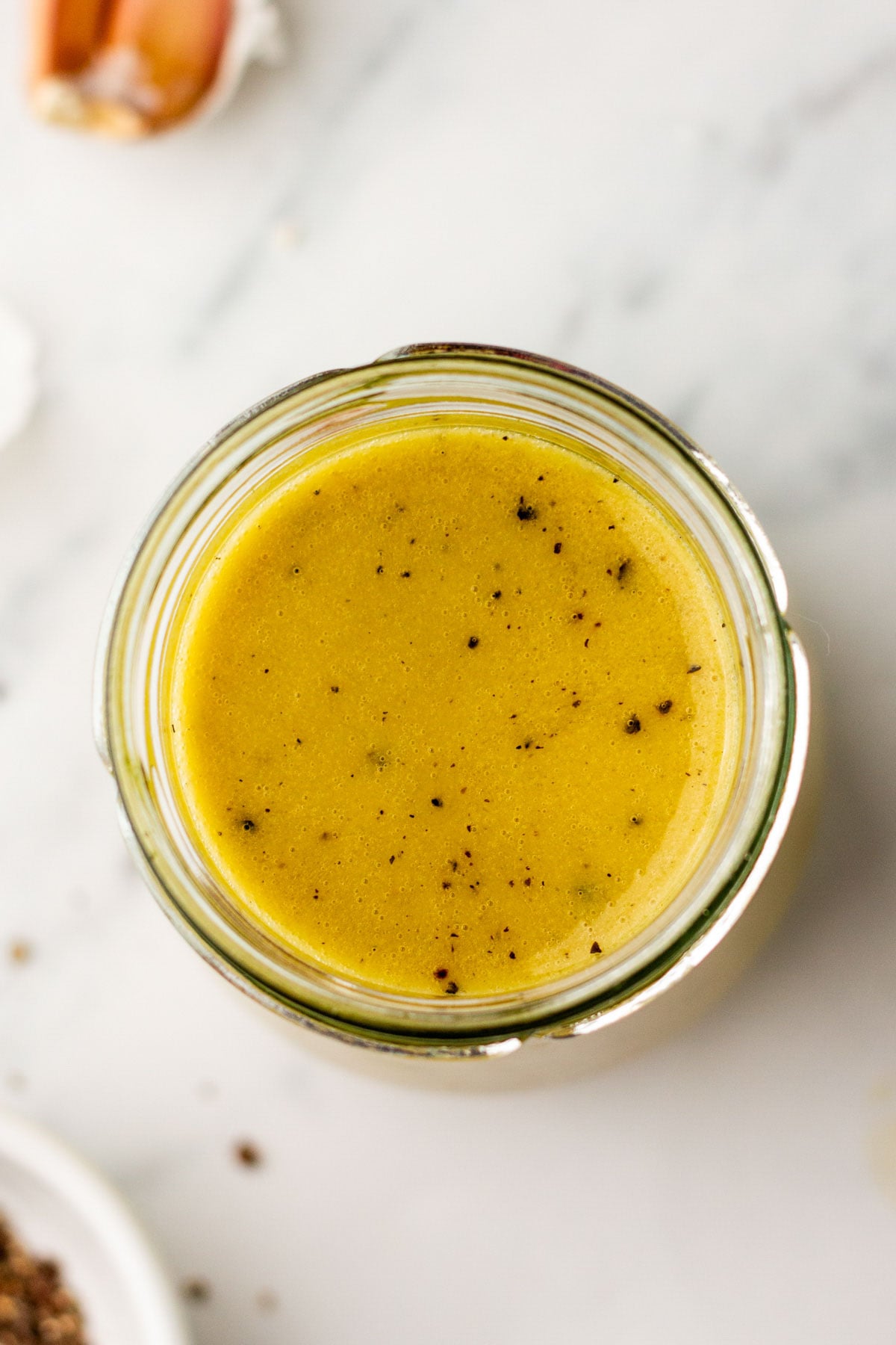 A clear glass jar filled with a homemade salad dressing sits on a marble surface.