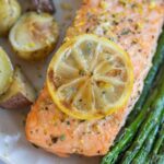 A plate with baked salmon topped with a lemon slice and lemon zest, roasted baby potatoes, and asparagus.