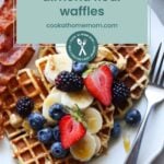 Plate of delicious Paleo Waffles crafted from almond flour, topped with sliced bananas, blueberries, strawberries, and blackberries. Served alongside crispy bacon for a perfect start. Text overlay promotes our website and invites you to explore the ultimate Waffle Bar experience.