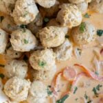Thai-flavored turkey meatballs garnished with herbs in a creamy sauce with sliced red onions and bell peppers.