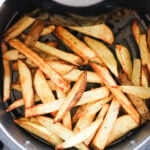 Golden-brown potato fries are evenly spread inside an air fryer basket.