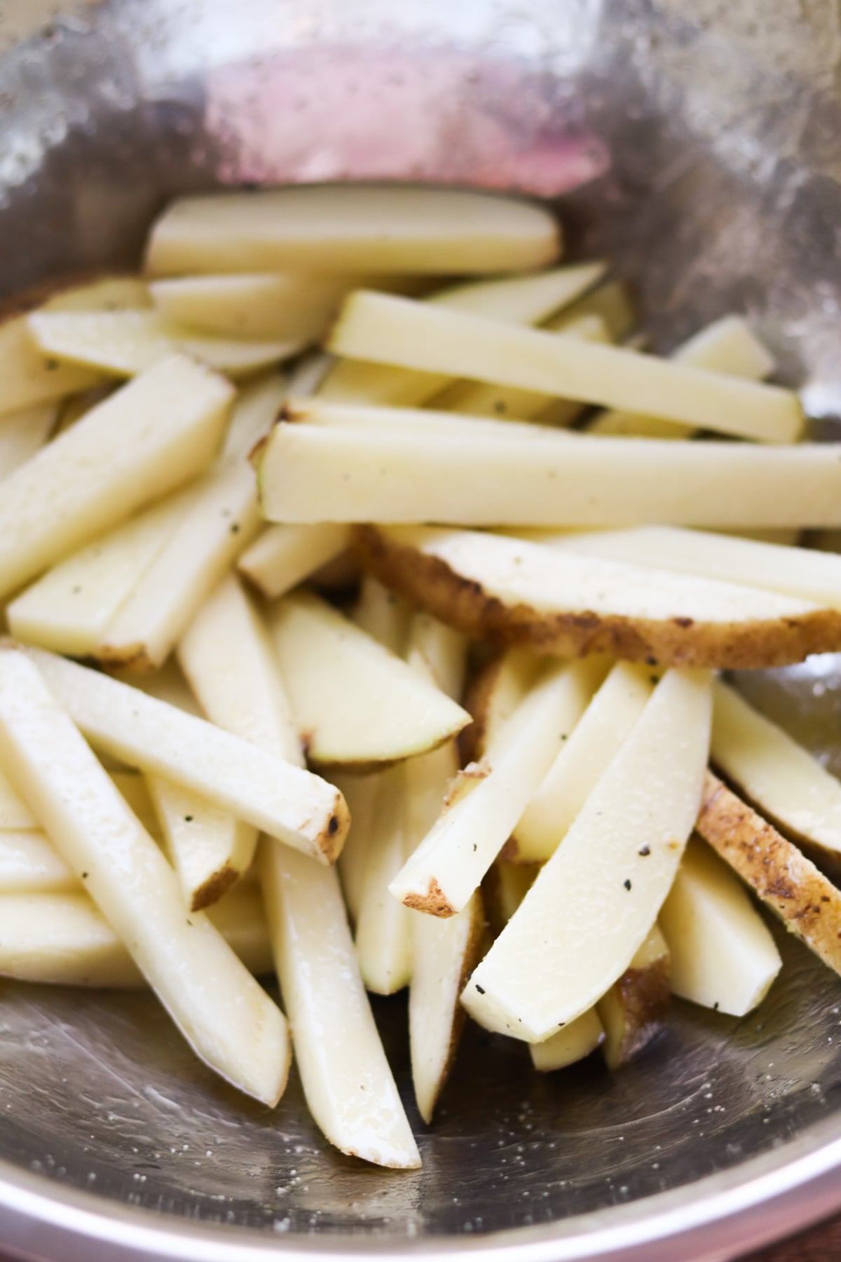 A bowl of raw potato wedges with skin, seasoned with pepper and salt.