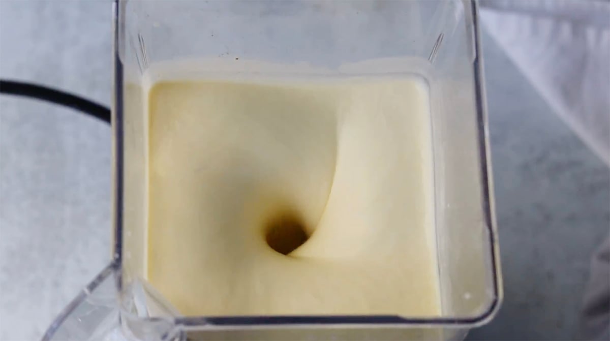 Top view of a blender mixing creamy batter, creating a vortex.