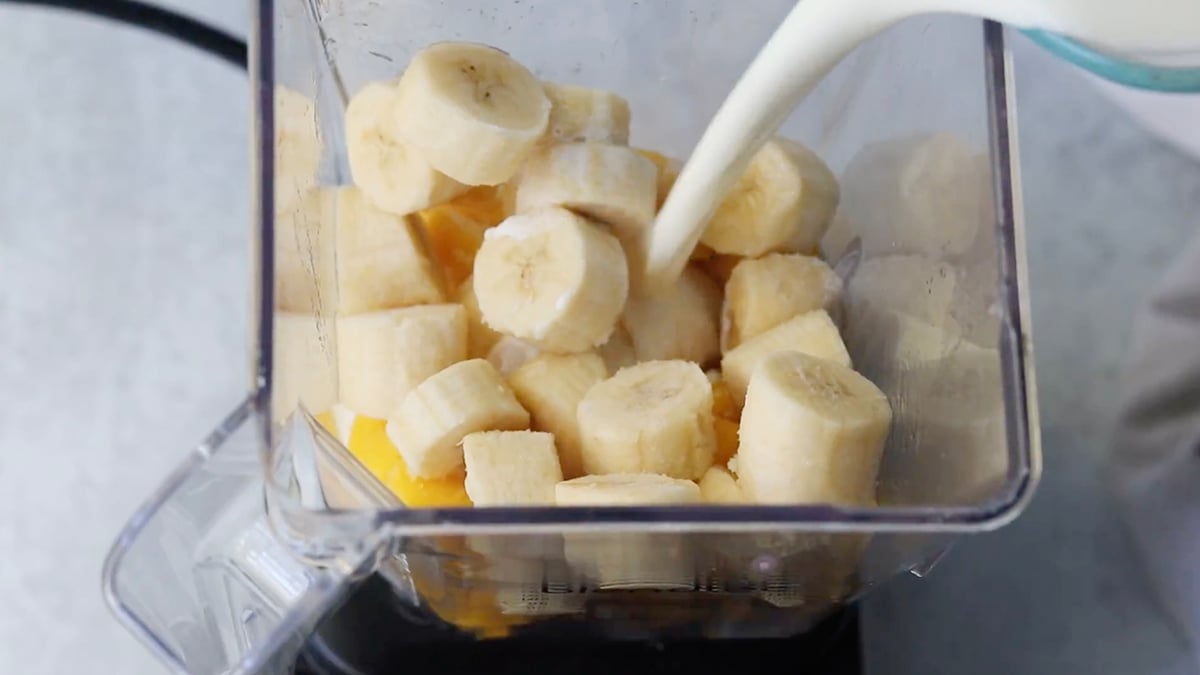 Sliced bananas and milk being poured into a blender.
