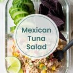 A glass meal prep container with sliced cucumber, blue corn tortilla chips, lime wedge, and Mexican tuna salad with corn and peppers—perfect for pairing with leftover Dutch oven chicken—sits next to a black fork.