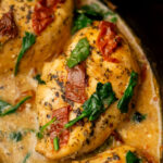 Close-up of cooked chicken breasts in a creamy sauce with wilted spinach and sun-dried tomatoes.