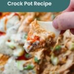 A hand holds a chip topped with buffalo chicken dip in front of a plate of the same dip, garnished with green onions and sauce. Text overlay reads "Buffalo Chicken Dip Crock Pot Recipe." Pairs perfectly with a refreshing paloma mocktail.