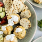A plate with grilled pita bread, rice, Greek chicken meatballs topped with white sauce, and a cucumber-tomato salad.
