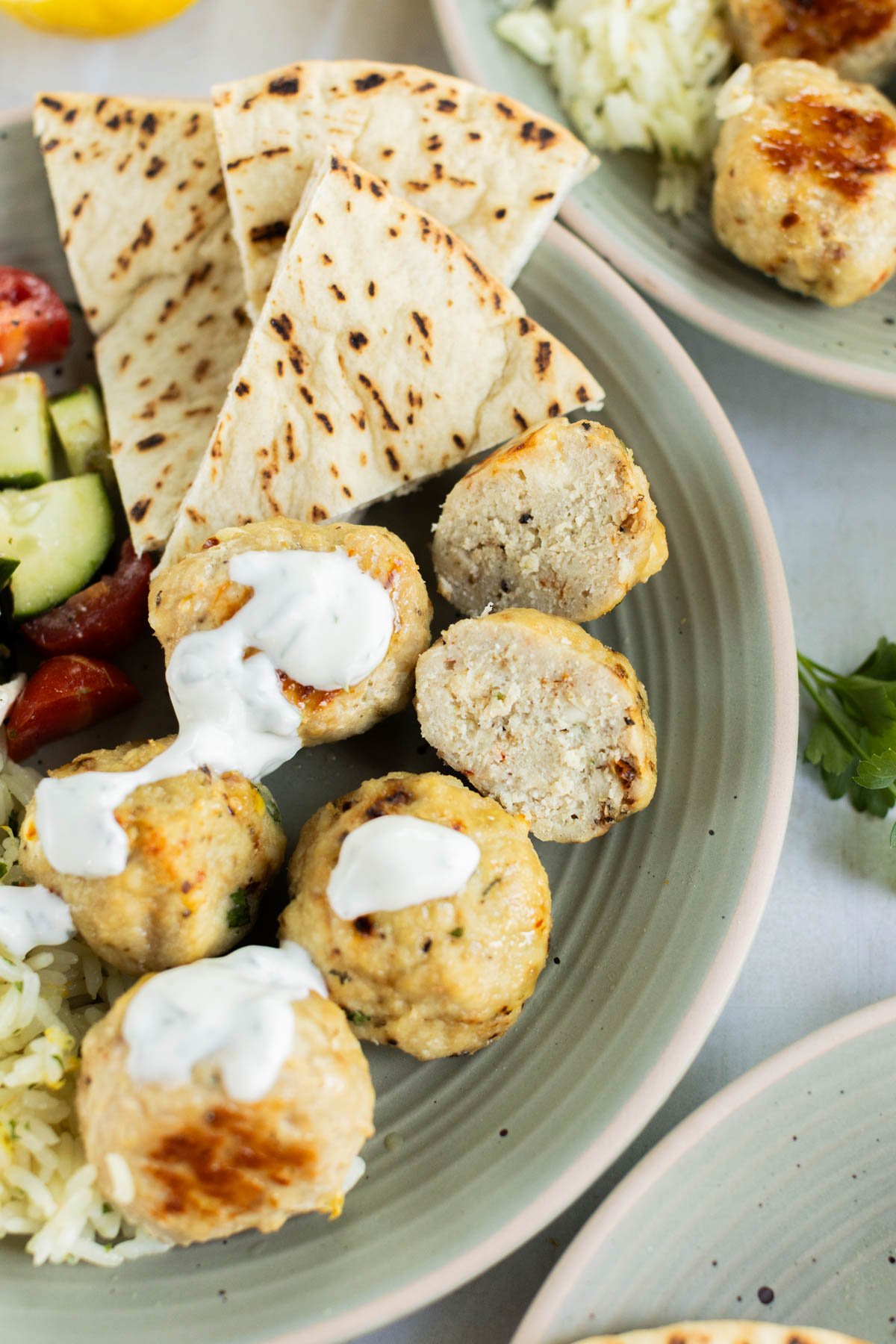 A plate with grilled pita bread, rice, Greek chicken meatballs topped with white sauce, and a cucumber-tomato salad.