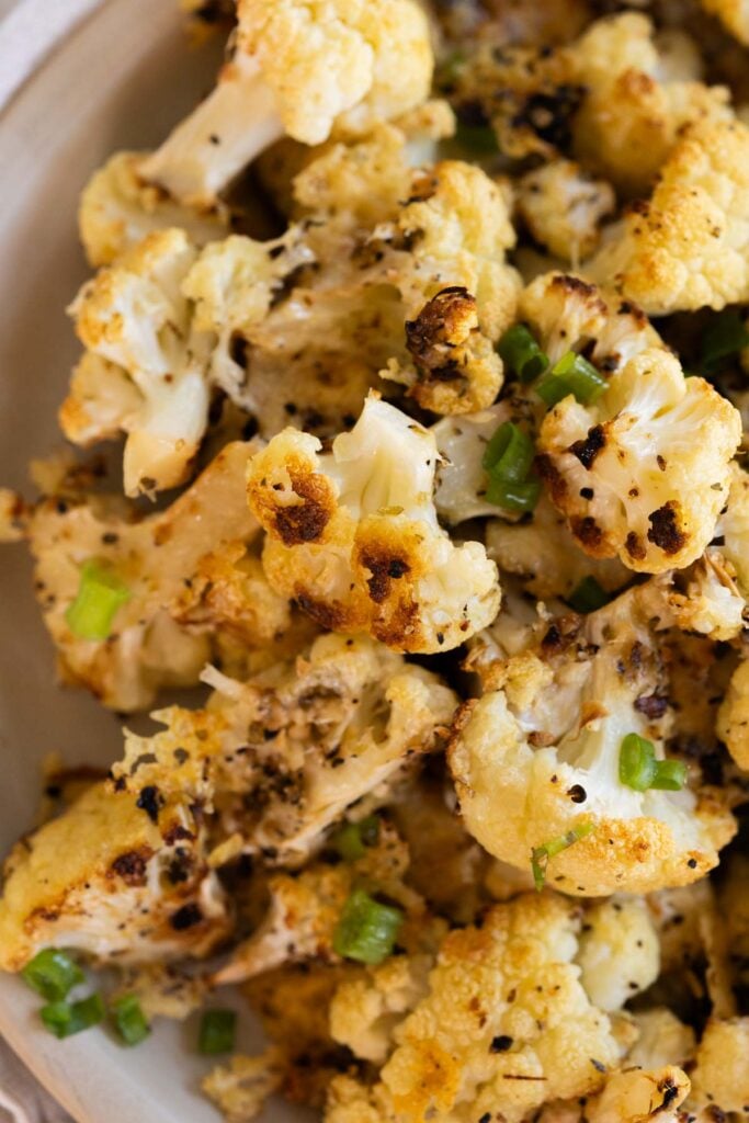 Close-up of roasted cauliflower florets garnished with chopped green onions, showing browned and crispy edges.