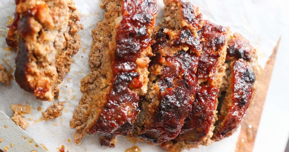 Sliced meatloaf with a glossy, dark glaze on top, arranged on parchment paper.