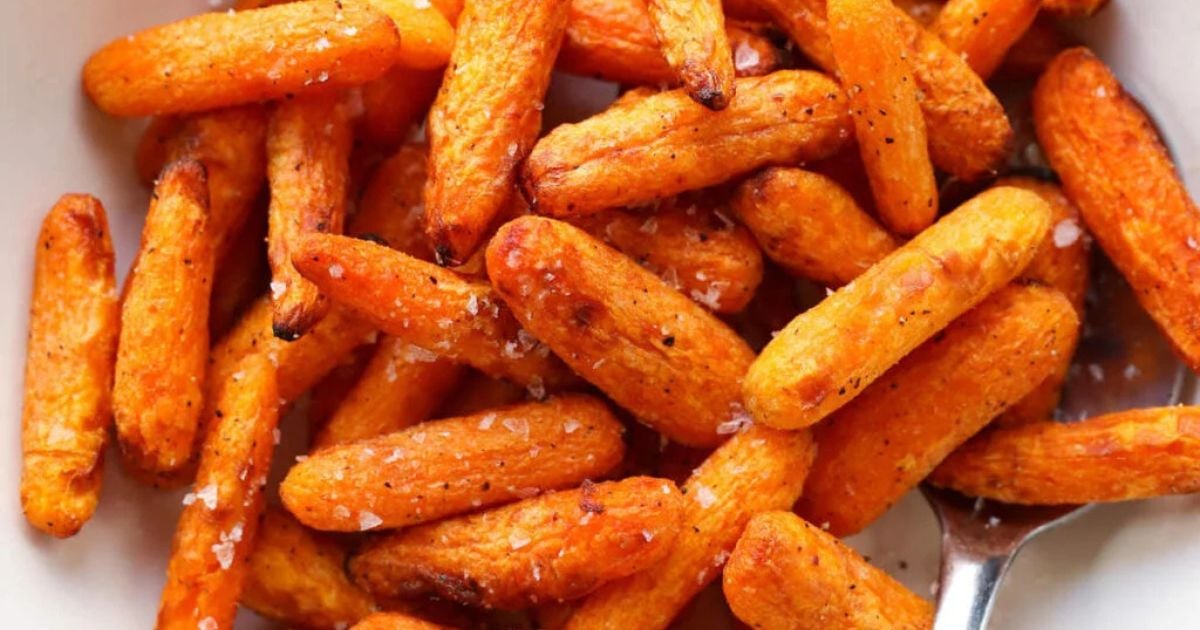 Close-up of roasted baby carrots seasoned with salt and pepper, served in a white bowl with a metal spoon.
