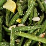 A dish of roasted green beans garnished with lemon wedges, lemon zest, and slivered almonds.