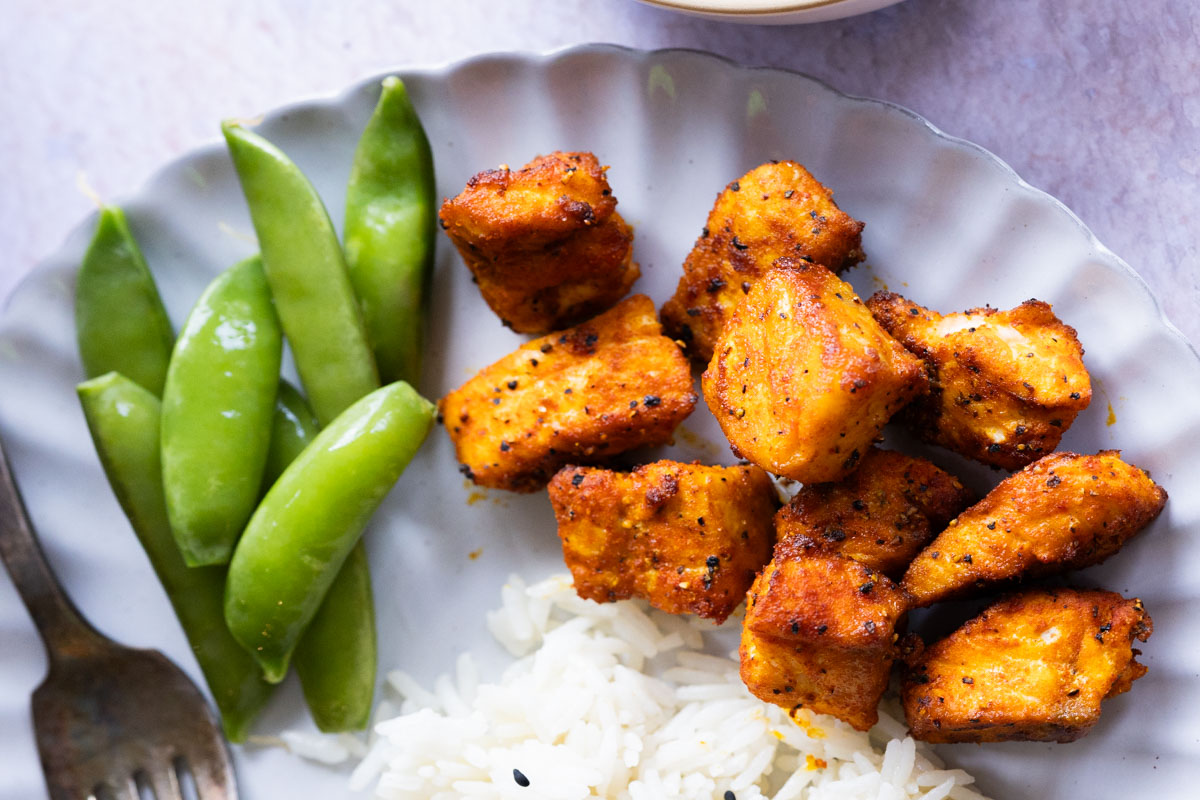 A plate with grilled air-fryer salmon bites, white rice, and snap peas, with a fork on the side.