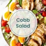 A bowl of Cobb salad with sliced grilled chicken, boiled eggs, cherry tomatoes, avocado, red onion, blue cheese, and lettuce—perfect for pairing with pork lettuce wraps. Text overlay reads “Cobb Salad.”.