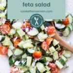 A bowl of cucumber tomato feta salad with red onion, served with a wooden spoon, overlaid with a label reading "cucumber tomato feta salad.
