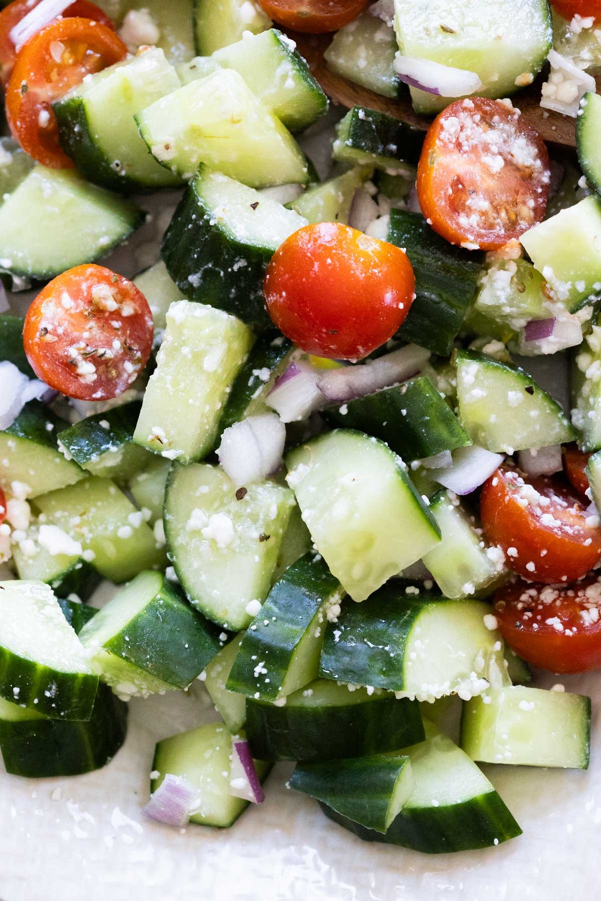 Chopped cucumber, cherry tomatoes, red onion, and crumbled cheese mixed together in a salad.