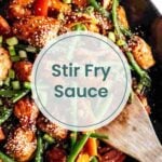 A pan of chicken and vegetable stir fry with sesame seeds and green onions, with a wooden spatula, highlights the rich flavors of stir fry sauce. The text "Stir Fry Sauce" is overlayed in the center.