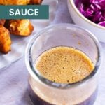 A jar of stir fry sauce sits on a countertop, with a plate of cooked chicken pieces and a bowl of vibrant purple cabbage in the background.