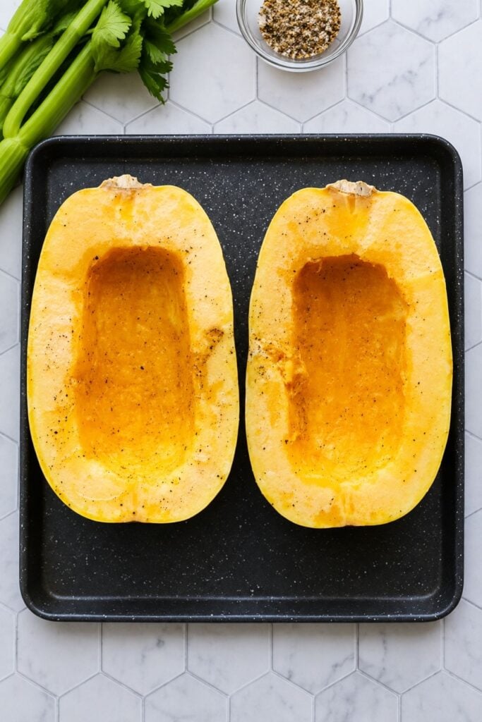 Spaghetti squash halves seasoned and ready to roast on a baking sheet.
