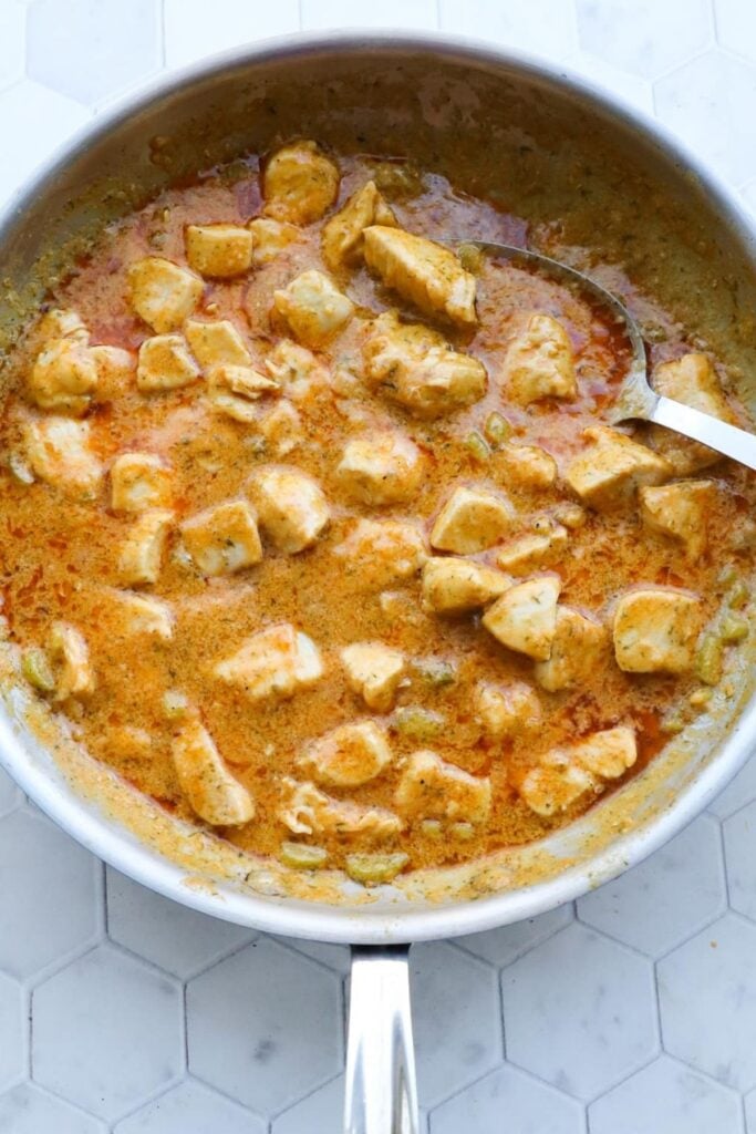 Buffalo chicken simmering in a creamy sauce in a skillet.