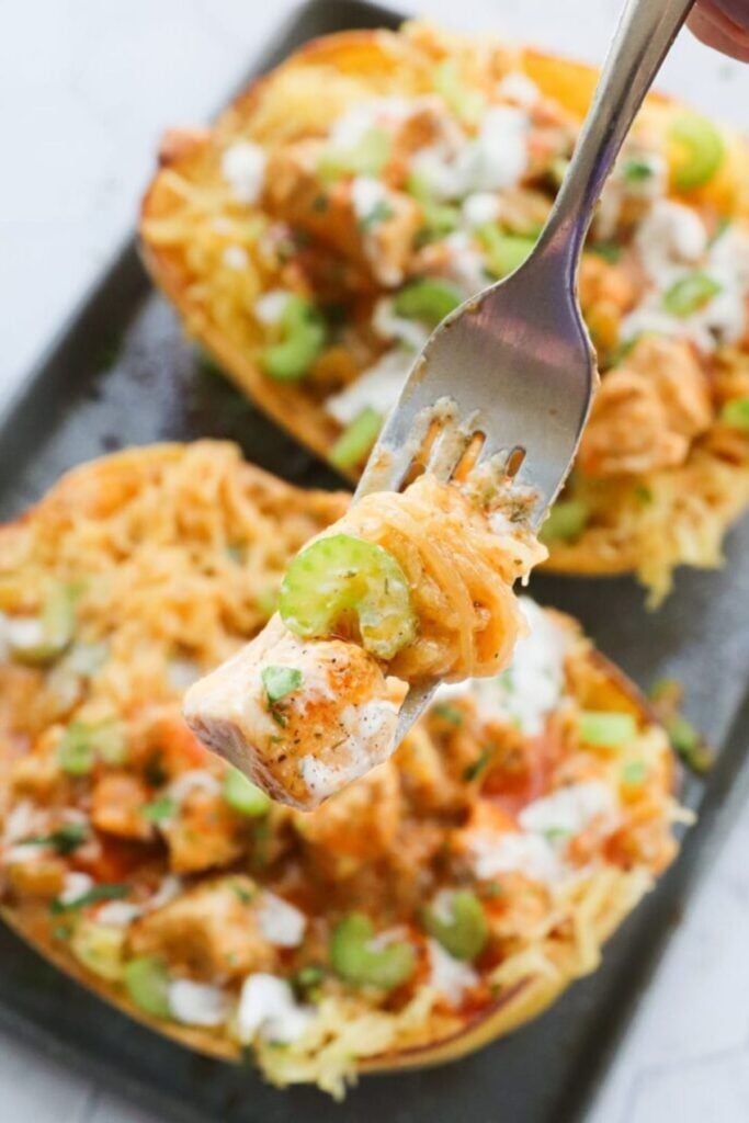 Forkful of buffalo chicken spaghetti squash with stuffed squash halves in the background.