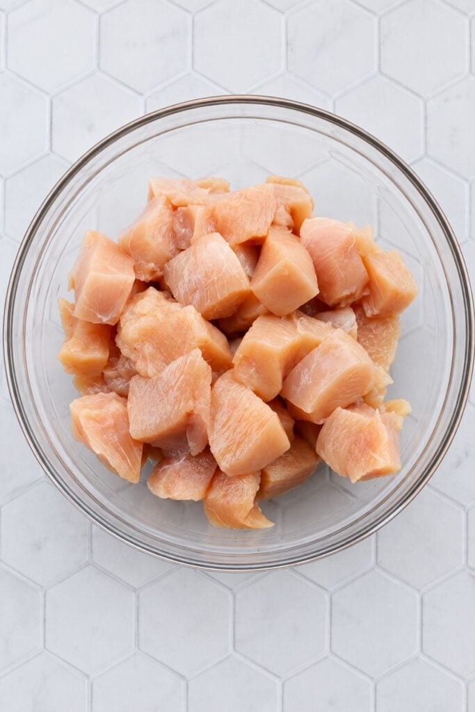 Raw chicken breast cut into bite-sized pieces in a glass bowl.