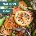 Oven baked salmon in foil, topped with a lemon slice, green onions, and black sesame seeds, served alongside fresh vegetables, with a fork in the foreground.