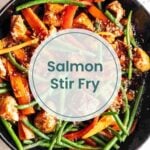 A skillet with cooked salmon pieces, green beans, carrot strips, and greek rice, viewed from above. Text overlay reads "Salmon Stir Fry.