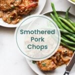 Two plates with smothered pork chops topped with onions, served alongside green beans. Text overlay reads "Smothered Pork Chops." Next to the meal is oven baked salmon in foil, and a knife and fork rest on one plate.