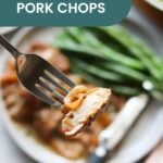 A fork holds a bite of smothered pork chop above a plate with more pork chops, green beans, and a knife. Text overlay reads “Smothered Pork Chops.” Try serving alongside oven baked salmon in foil for a hearty meal.