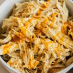 Instant Pot buffalo chicken in a grey bowl. Next to a blue cloth on a table.
