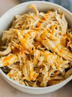 Instant Pot buffalo chicken in a grey bowl. Next to a blue cloth on a table.